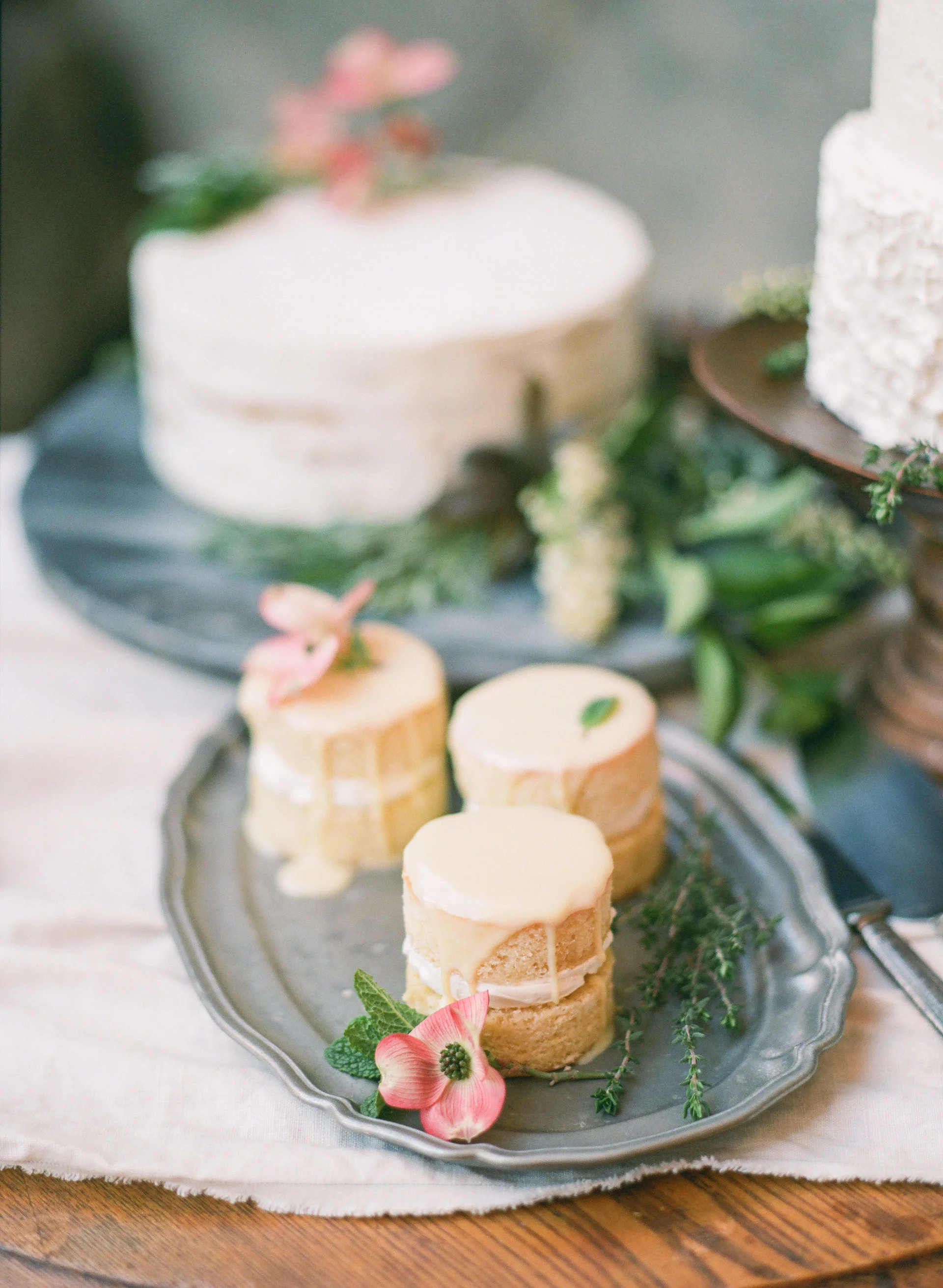 Three small frosted cakes topped with flowers on a metal tray, soft romantic mood