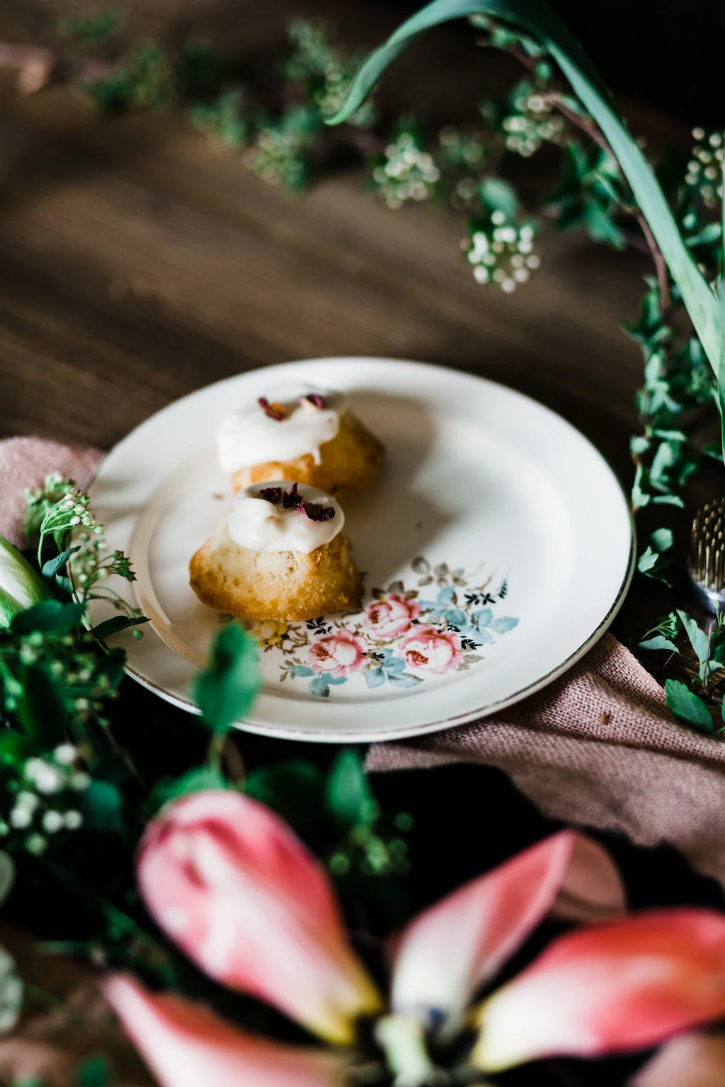 Two glazed pastries with dried flower garnish on a vintage floral plate